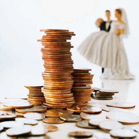 Stack of Coins and Bride and Groom Wedding Cake Decorations — Image by © Corbis