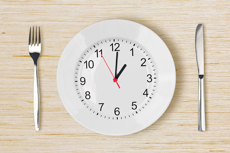 Dinner plate with clock face on wooden table with fork an knife