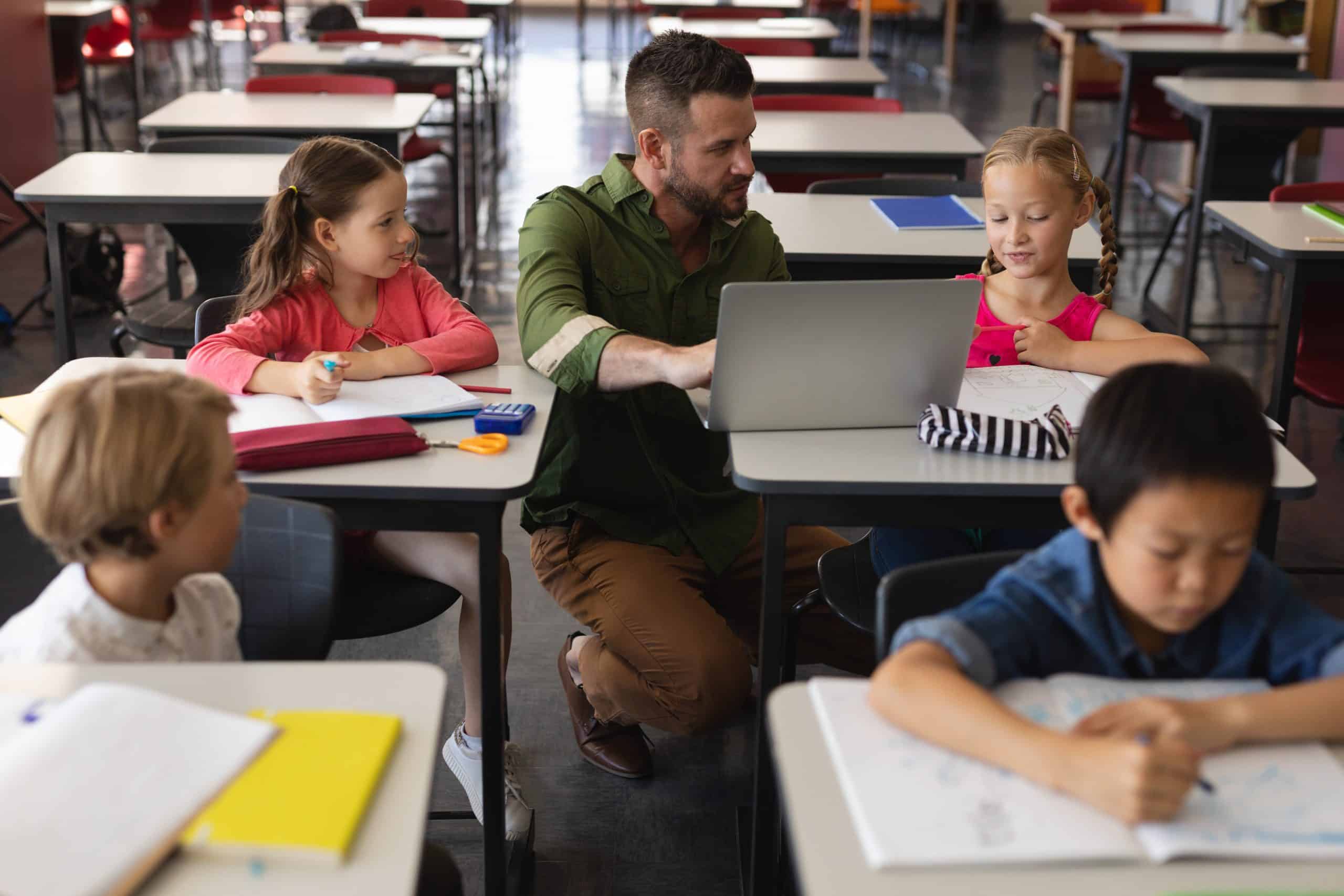 Front view of young school teacher helping girl with study on laptop in classroom