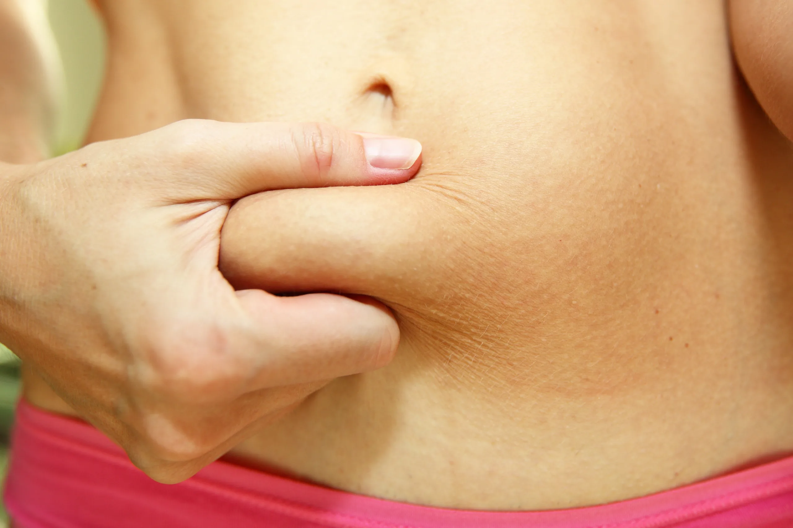 A close-up image of a slim young woman with a belly fat after giving birth. Woman’s torso with some belly fat. Abdominal fat.