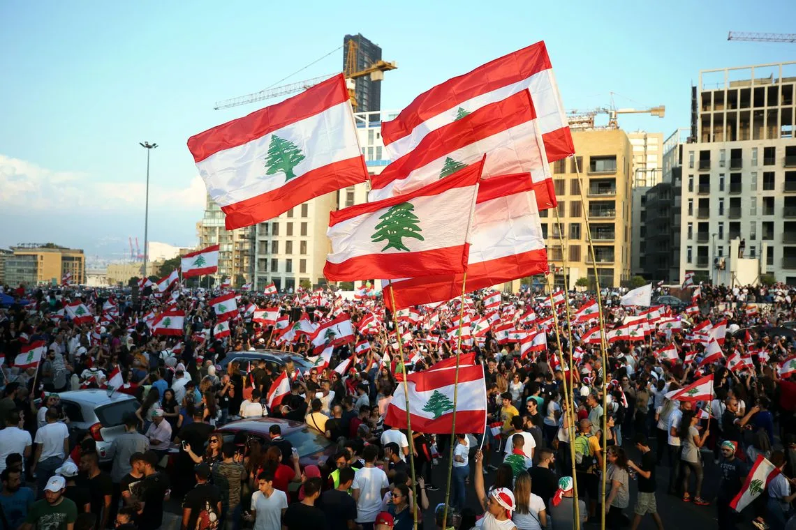 Manifestantes carregam bandeiras nacionais durante um protesto contra o governo no centro de Beirute, Líbano, em 20 de outubro de 2019