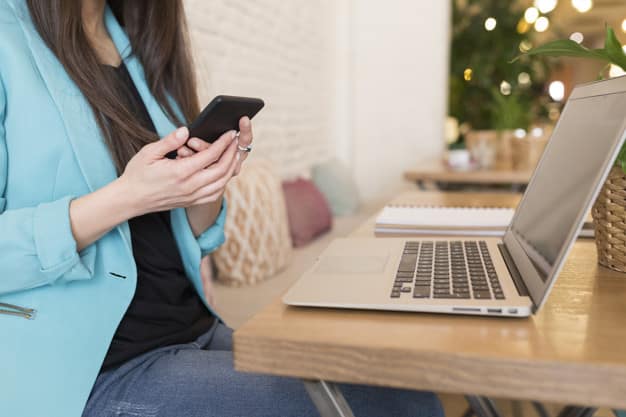 portrait of an unrecogniceable woman using mobile phone in a restaurant. Modern life of a blogger with computer laptop, tablet, notebook and coffee on table. Casual clothes. Lifestyle