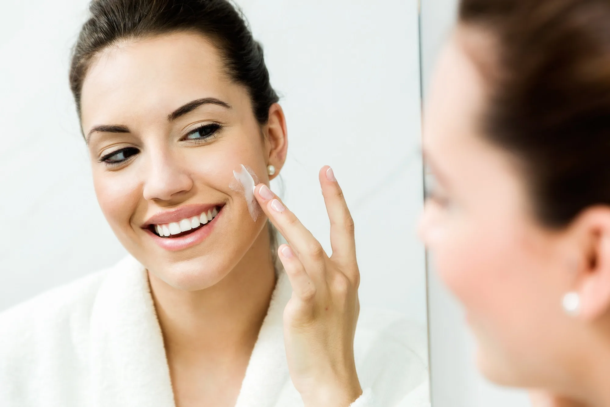 Portrait of young woman caring of her skin standing near mirror in the bathroom.