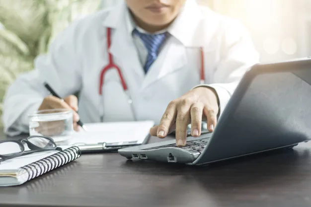 doctor searching information from computer and writing on notebook on working table