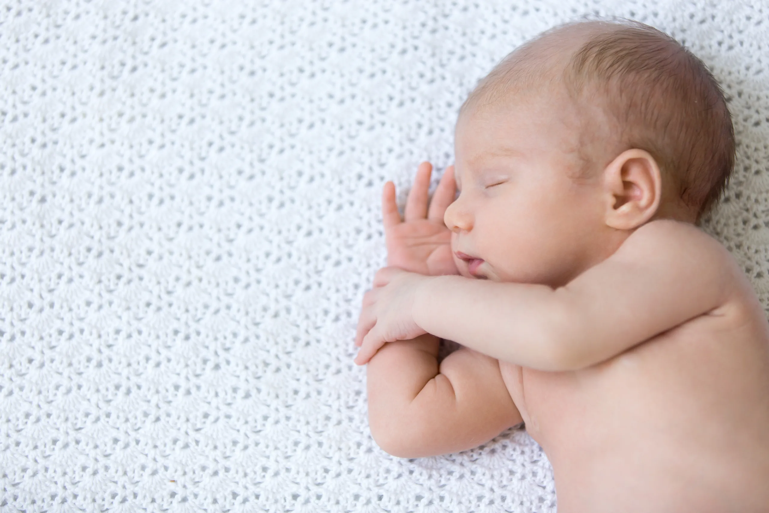 Portrait of young funny newborn babe napping on white knitted blanket. Cute caucasian new born child sleeping. Healthy one month old kid lying on bed with closed eyes. Close-up. View from above