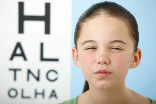 Girl squinting with eye chart in background — Image by © Image Source/Corbis