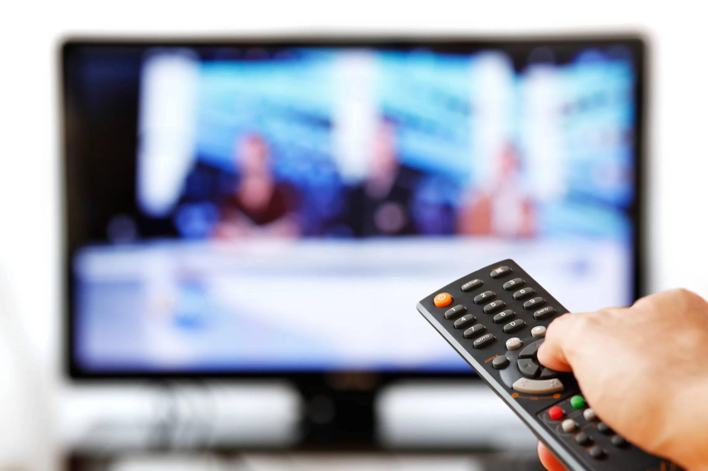 Out of focus TV LCD set and remote control in man’s hand isolated over a white background.