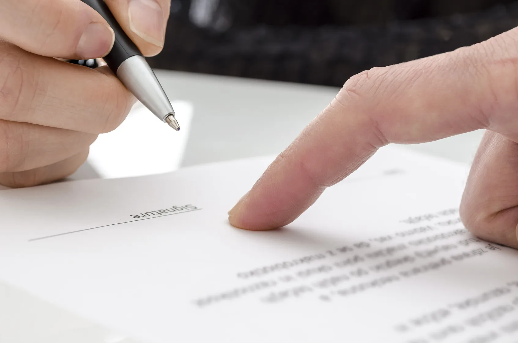 Detail of a woman signing a paper. Male finger showing where to sign.