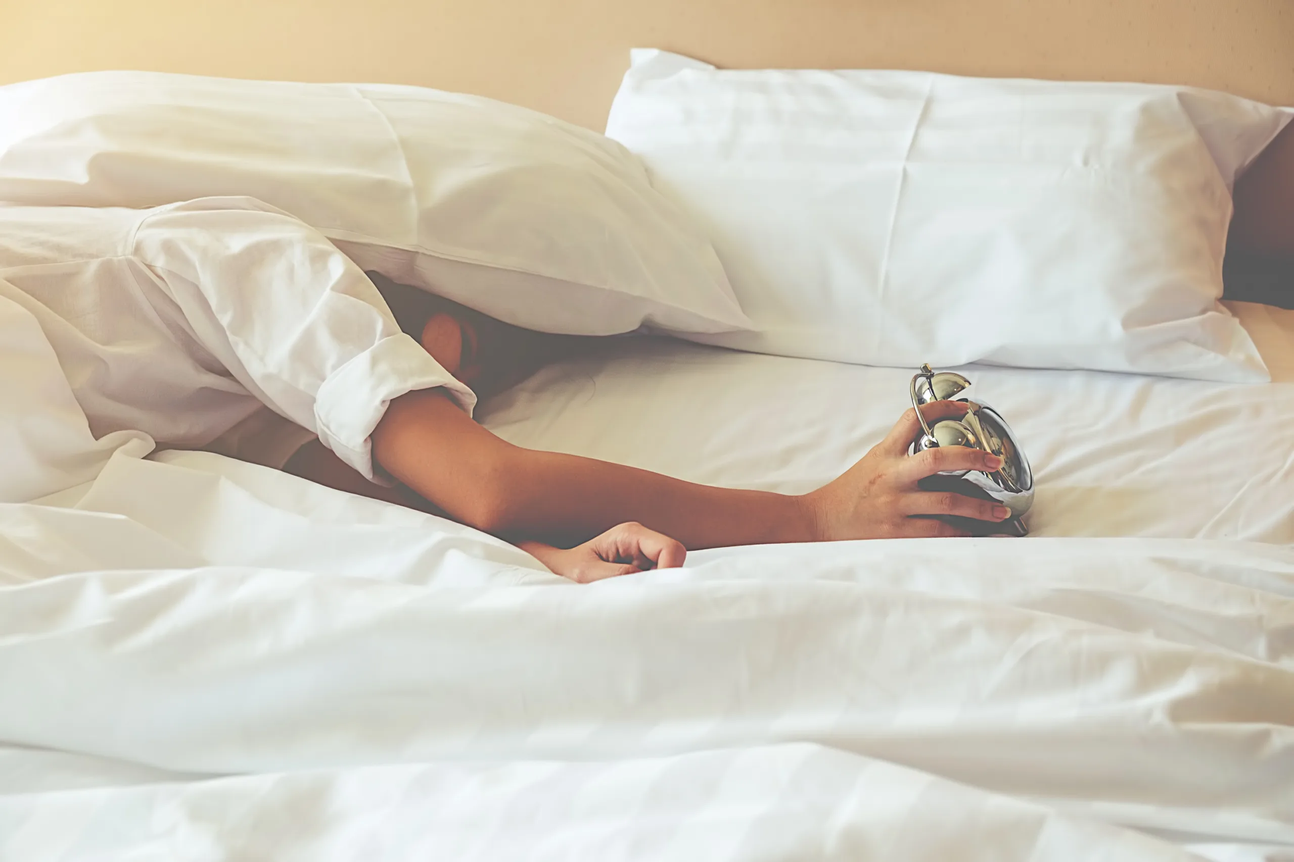 Irritated young woman putting her alarm clock off in the morning with soft morning light. Relaxing concept.