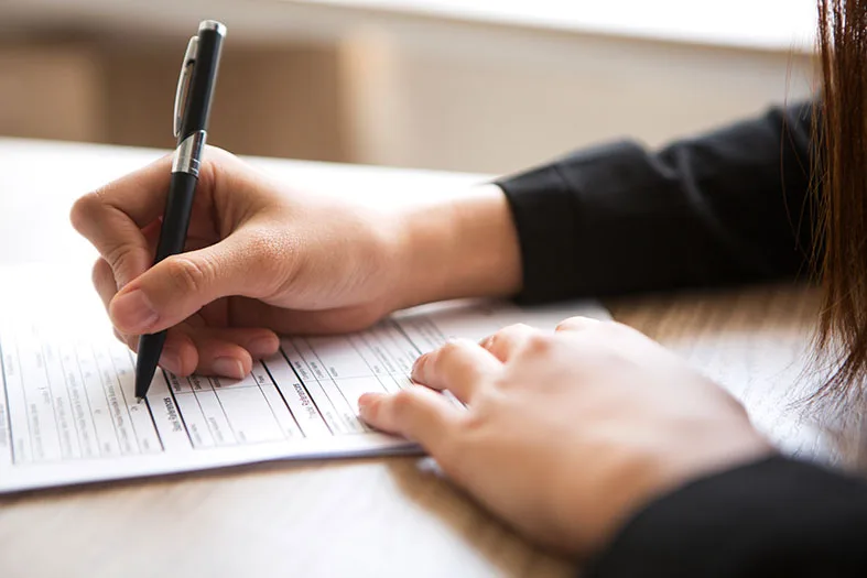 Cropped view of woman holding pen and filling in application form at table