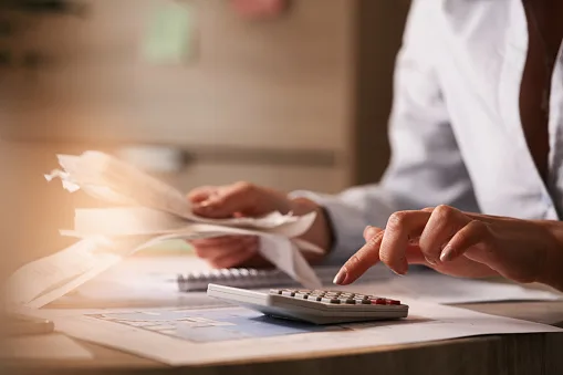 Close up of accountant holding bills and working on calculator in the office.