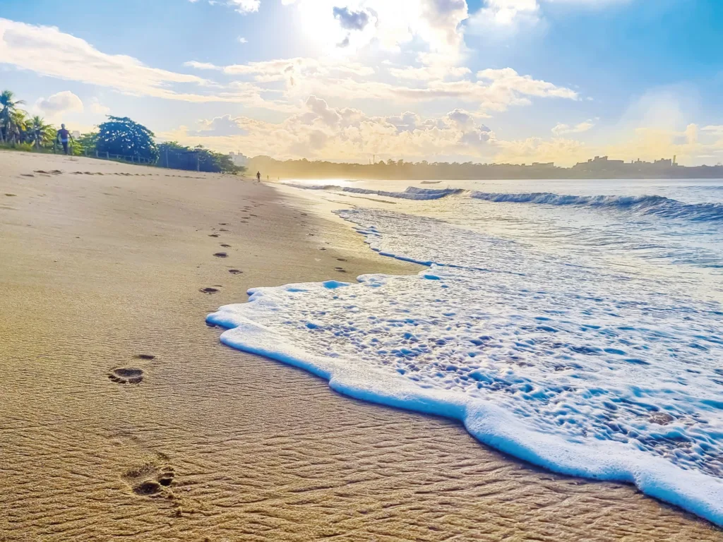 Praia de Camburi com pegadas humanas na areia, simbolizando a interação entre humanos e a natureza