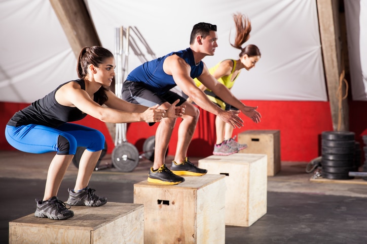 Group of athletic people jumpin over some boxes in a cross-training gym