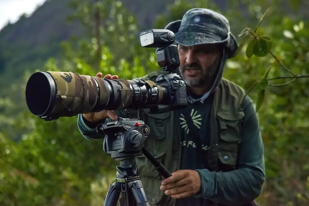 Fotógrafo de natureza usando lente teleobjetiva em um tripé para capturar imagens do ambiente natural.