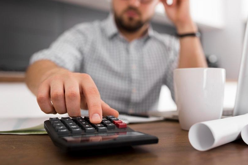 Imagem mostra homem fazendo contas em calculadora.