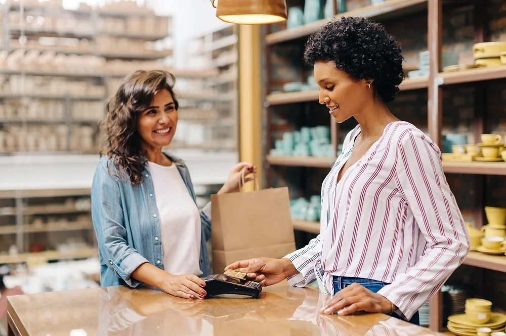 Happy ceramic shop owner scanning a credit card on a card machine to receive a payment. Cheerful small business owner doing a contactless transaction while serving a customer at checkout.