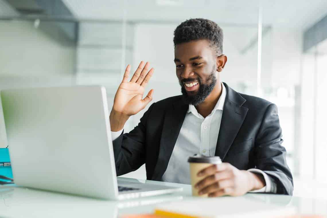 Young African manager with stubble sitting in front of open laptop wearing earphones while having video conference call with business partners