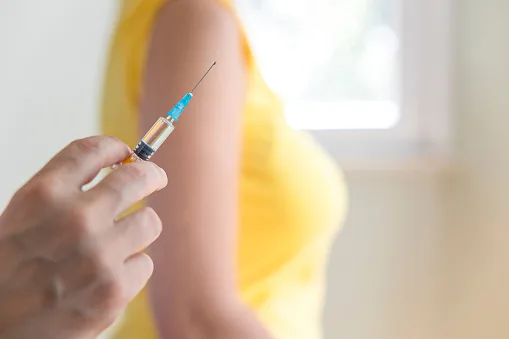 Doctor’s hand holding a vaccine and his patient on background