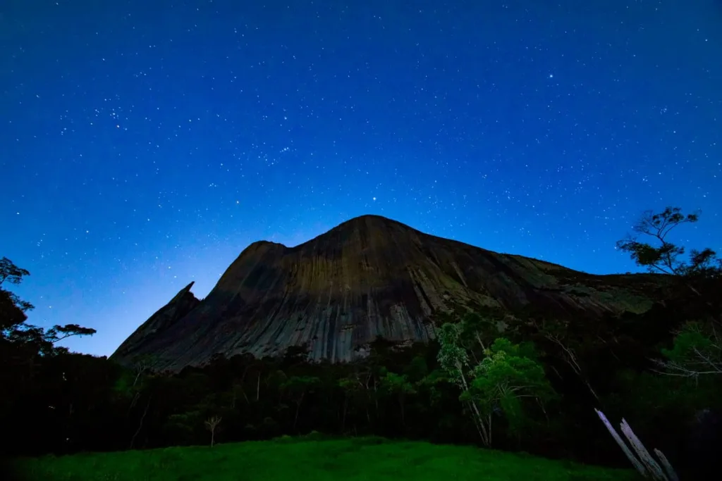 A Pedra Azul iluminada pelo luar contra um céu estrelado, vista de um ângulo único que revela sua parte traseira.