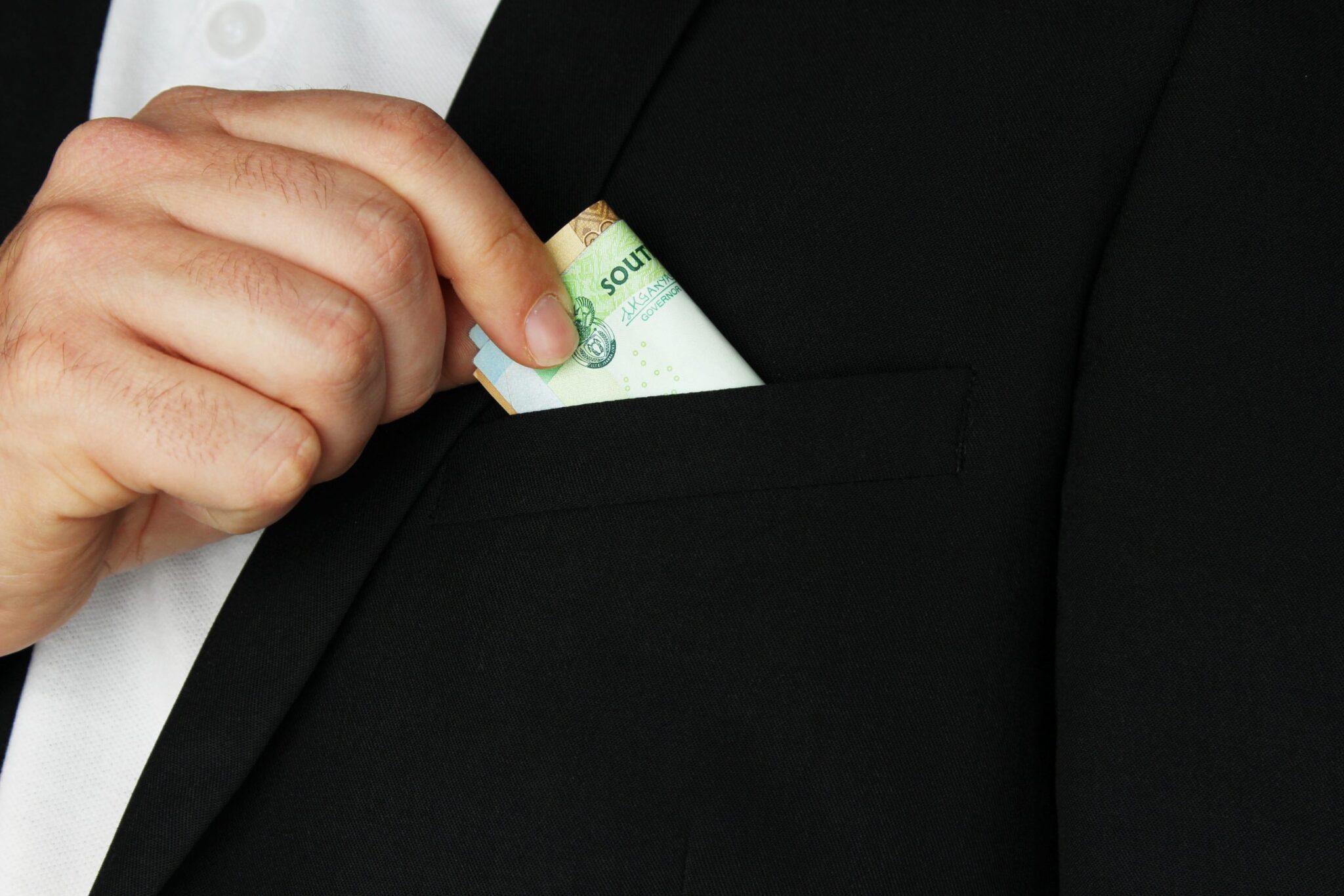 A closeup shot of a person putting some cash in the pocket of his coat