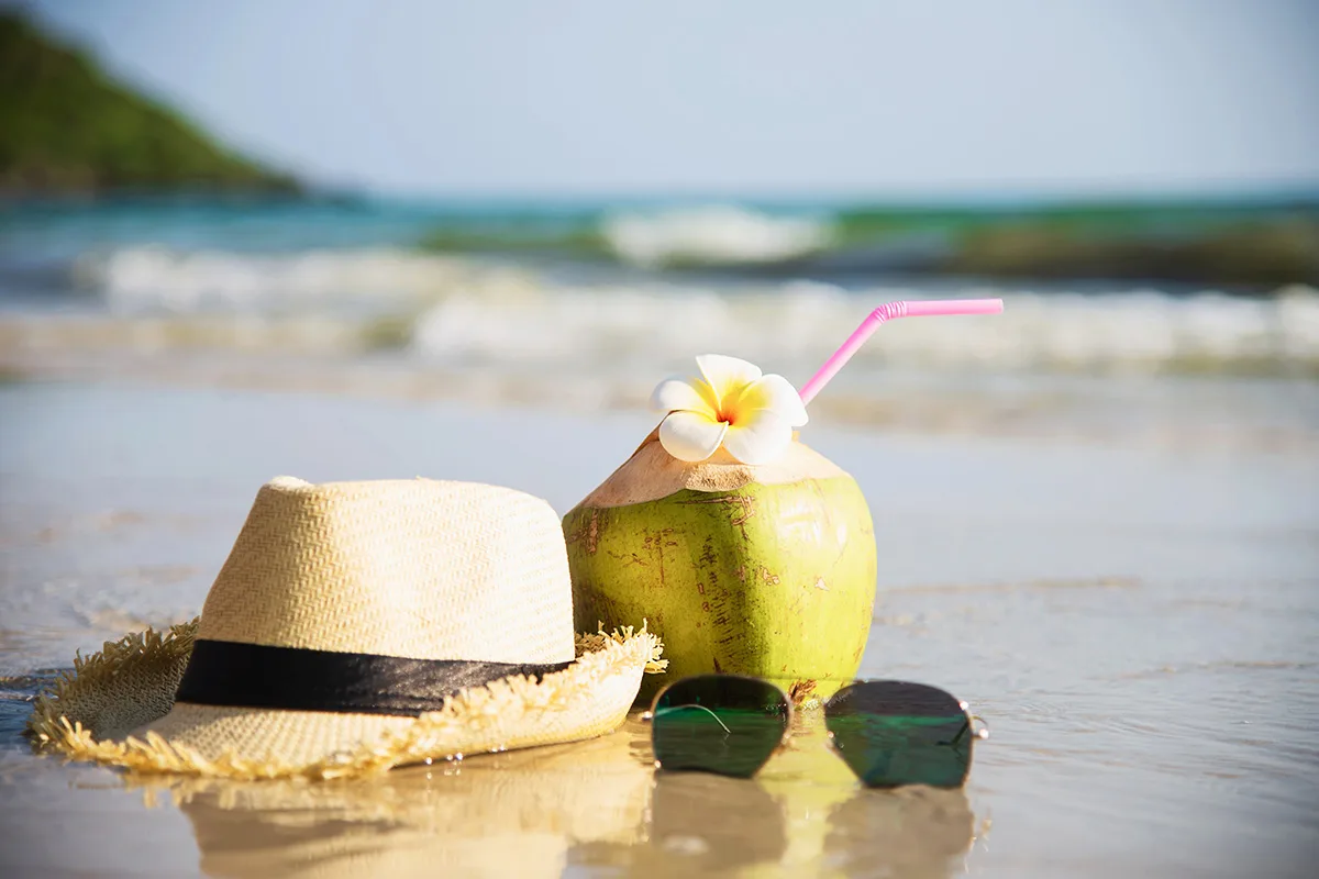 Fresh coconut with hat and sun glasses on clean sand beach with sea wave background – fresh fruit with sea sand sun vacation background concept