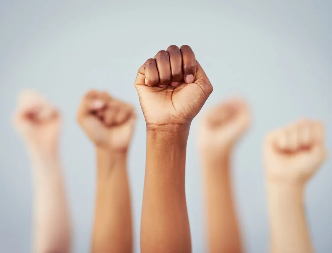 Cropped studio shot of a group of women raising their fists in solidarity against a gray background