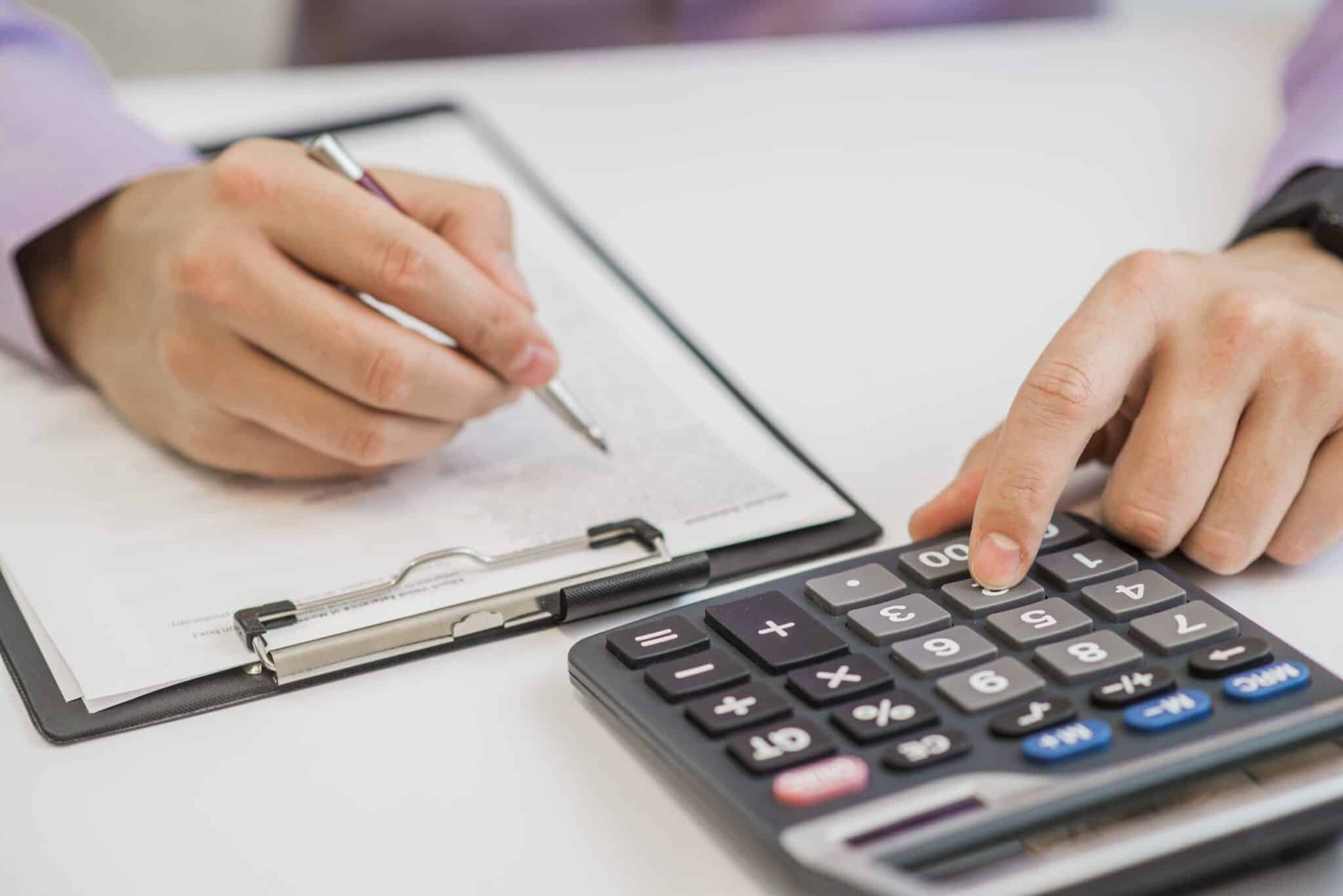 Close-up Of Businessman Calculating Invoices Using Calculator