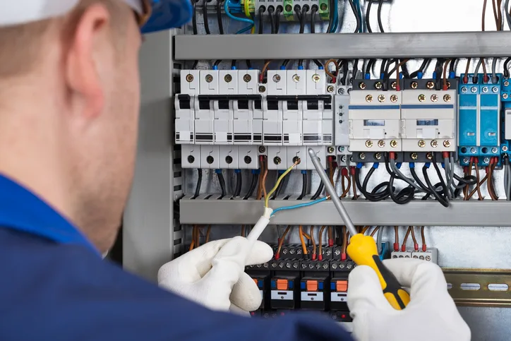 Male Electrician Working On Fusebox With Screwdriver