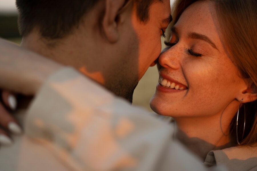 Casal se abraçando bem de perto, parecendo estar no pôr do sol.