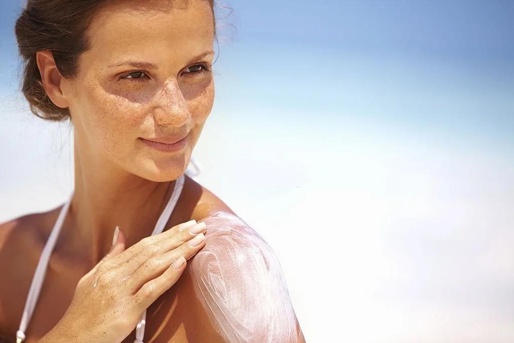 Closeup of lovely young woman applying sunscreen lotion on body