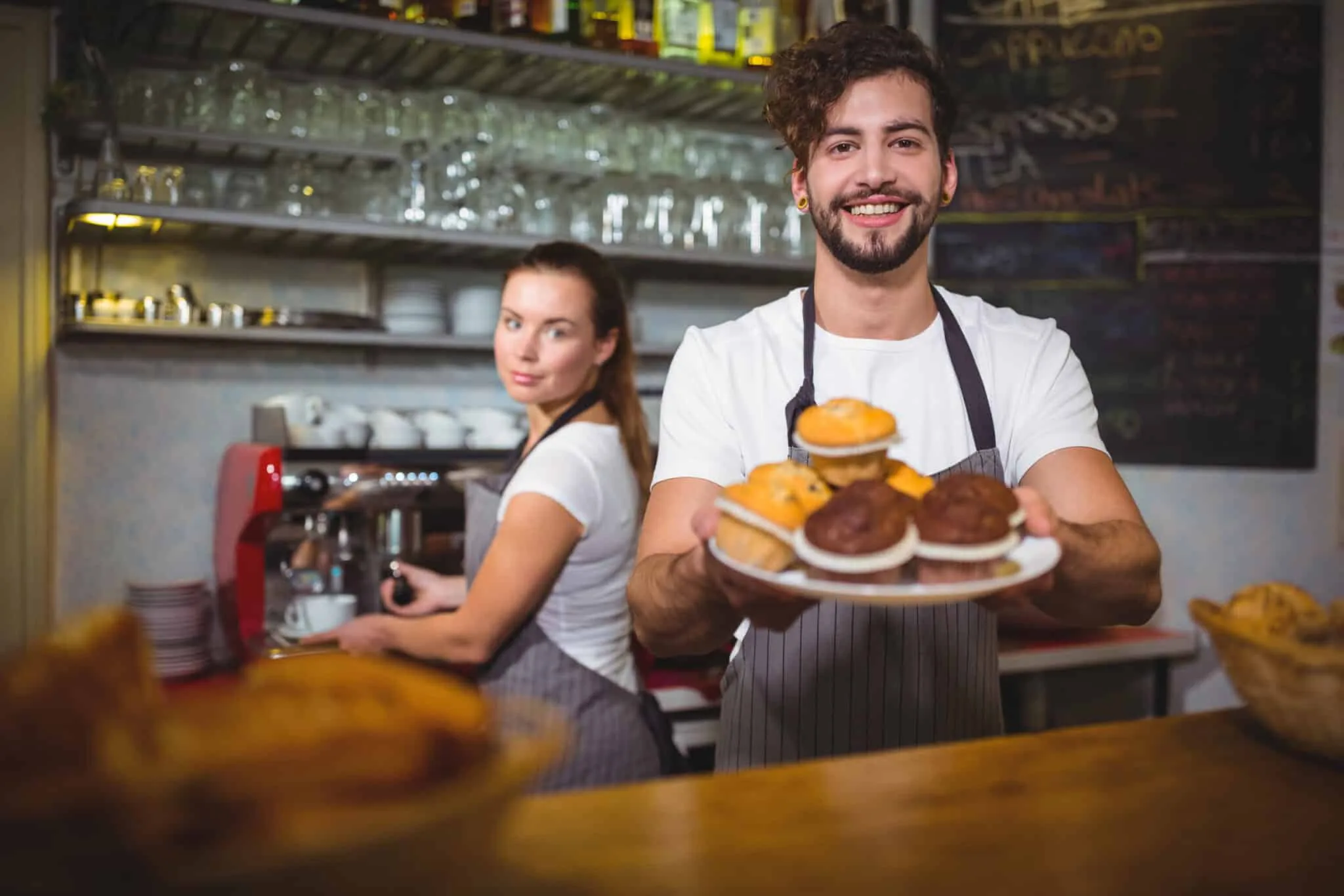 Portrait of waiter holding a plate of cup cake at counter in cafÃƒÂ©