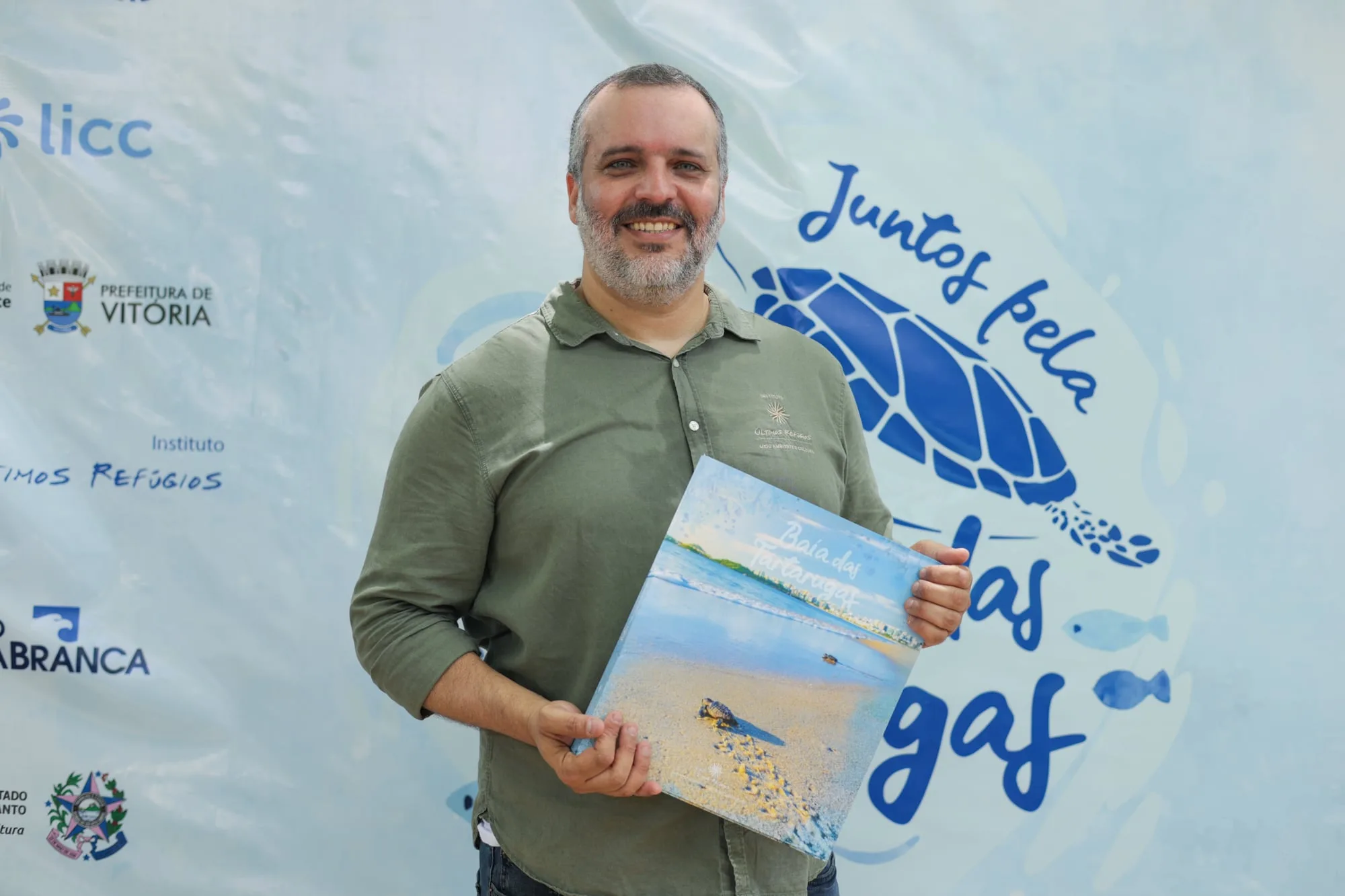 Fotógrafo Leonardo Merçon segurando o livro "Baía das Tartarugas" durante o evento de lançamento