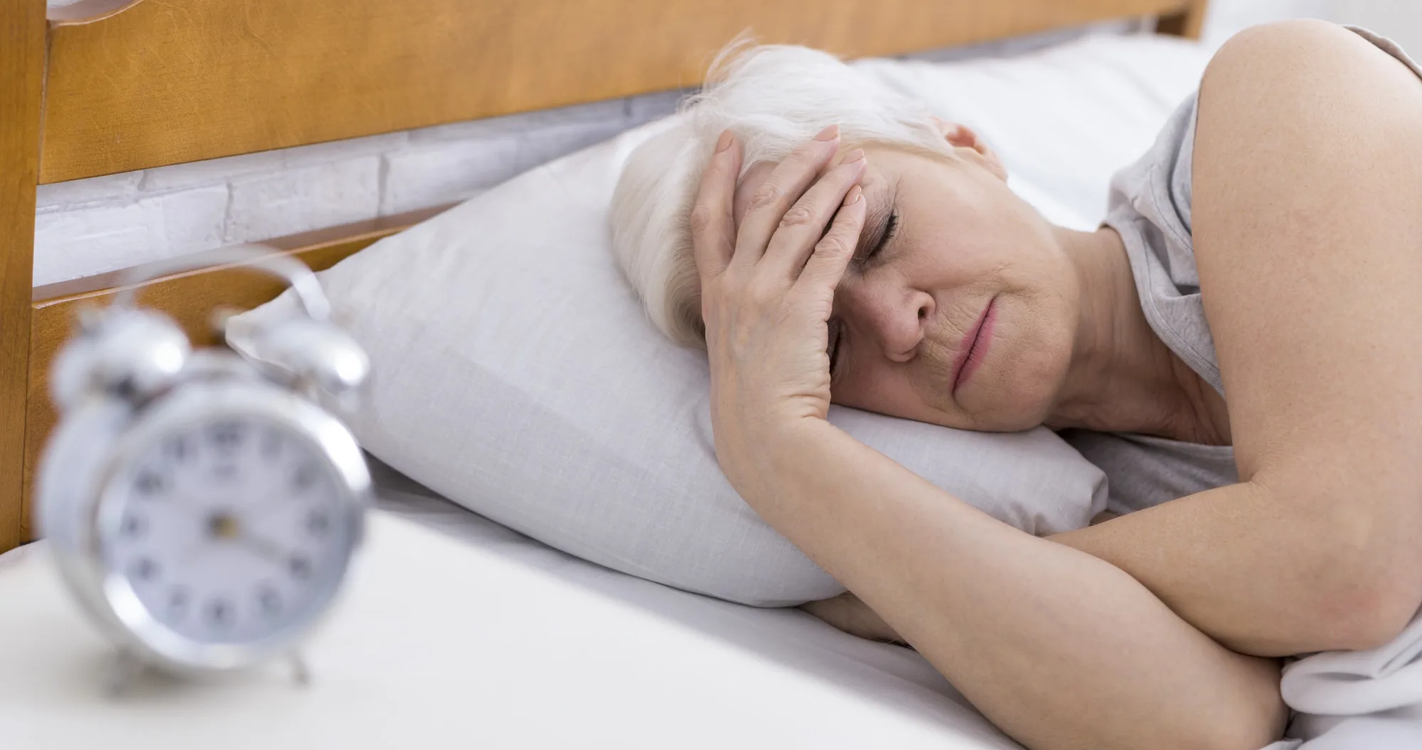 Worried senior woman suffering from insomnia, having headache in bed, touching her forehead, panorama