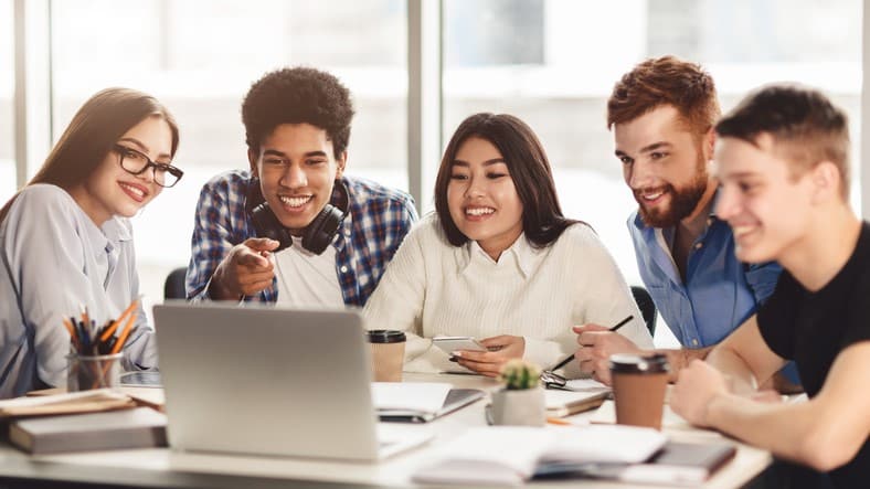 Group of multiracial students studying in library using laptop, preparing for exams together