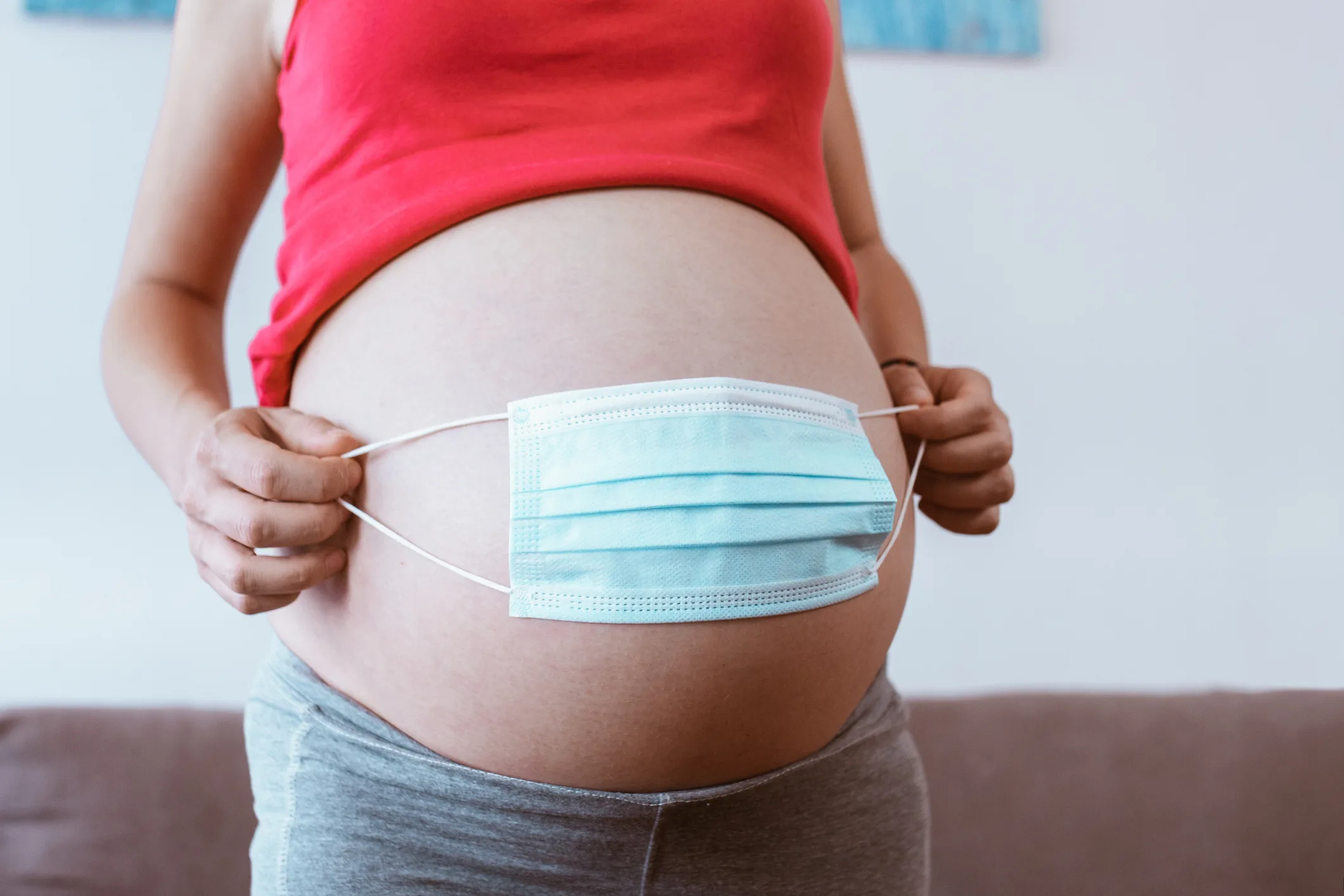 Close-up pregnant woman’s belly and medical mask. Concept of protection and prevention during pandemic, expectant mother and her baby health