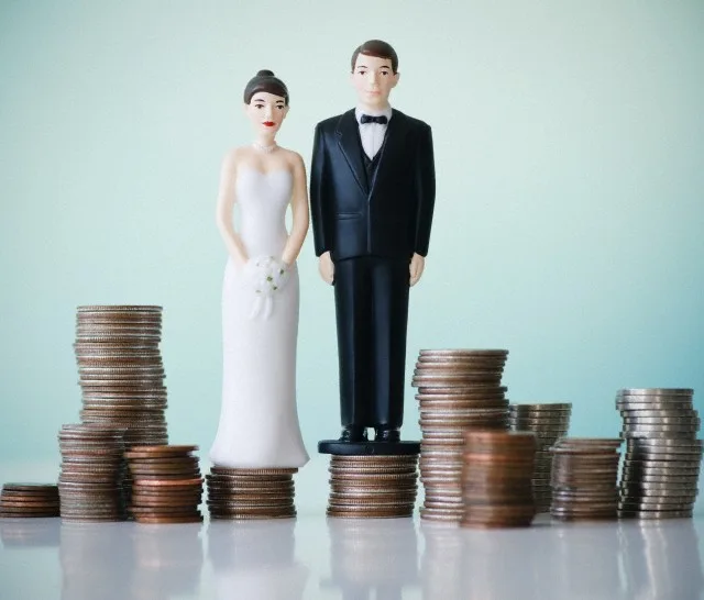 Close up of wedding cake figurines on stacks of coins — Image by © Tetra Images/Corbis