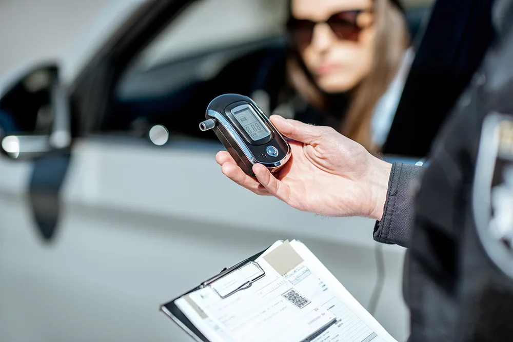 Policeman holding device for checking alcohol intoxication while standing near the stopped car with woman driver