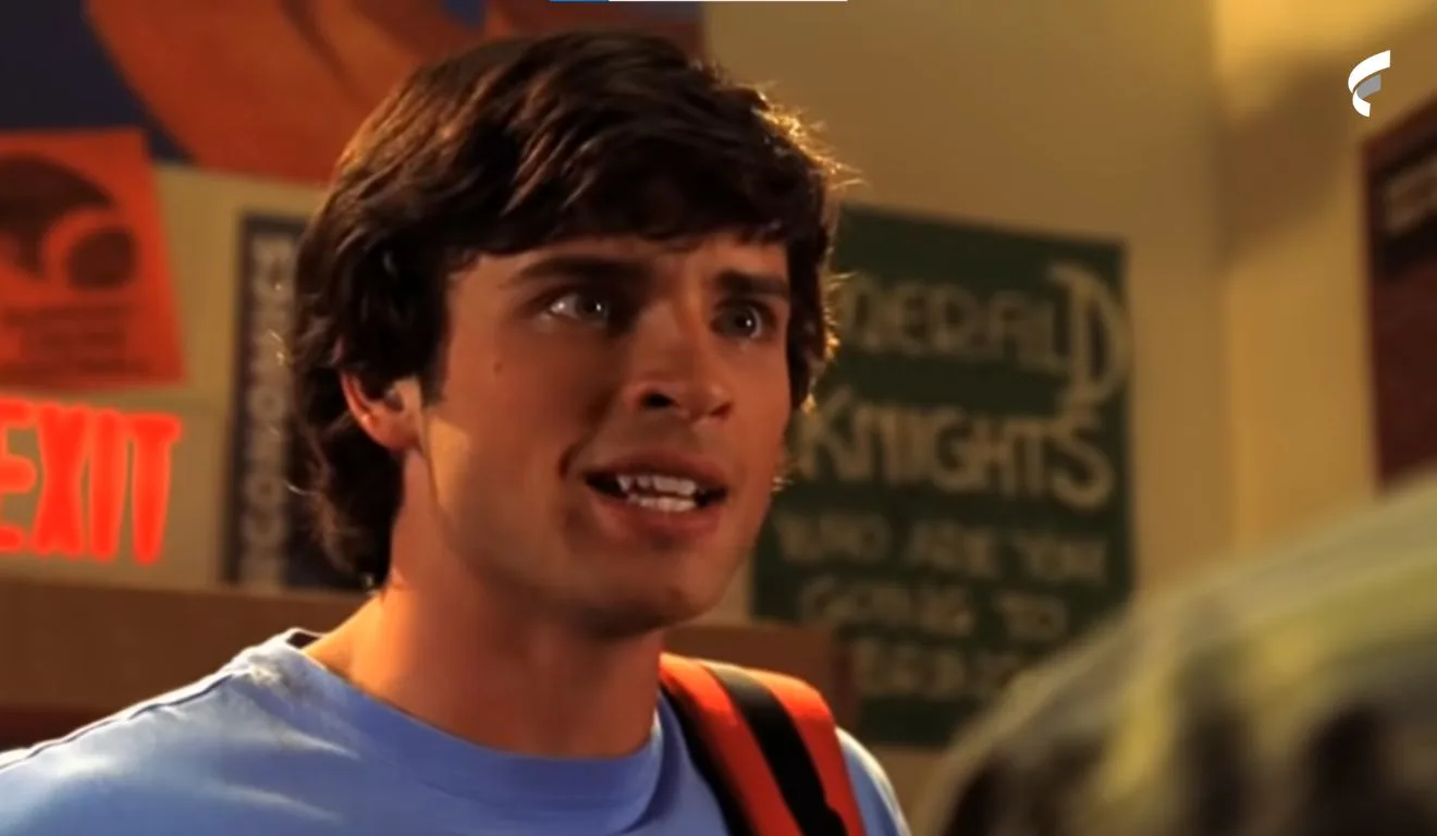 Tom Welling atuando em Smallville. Ele tinha cabelo curto, caindo na testa. Na foto, ele usa uma blusa azul