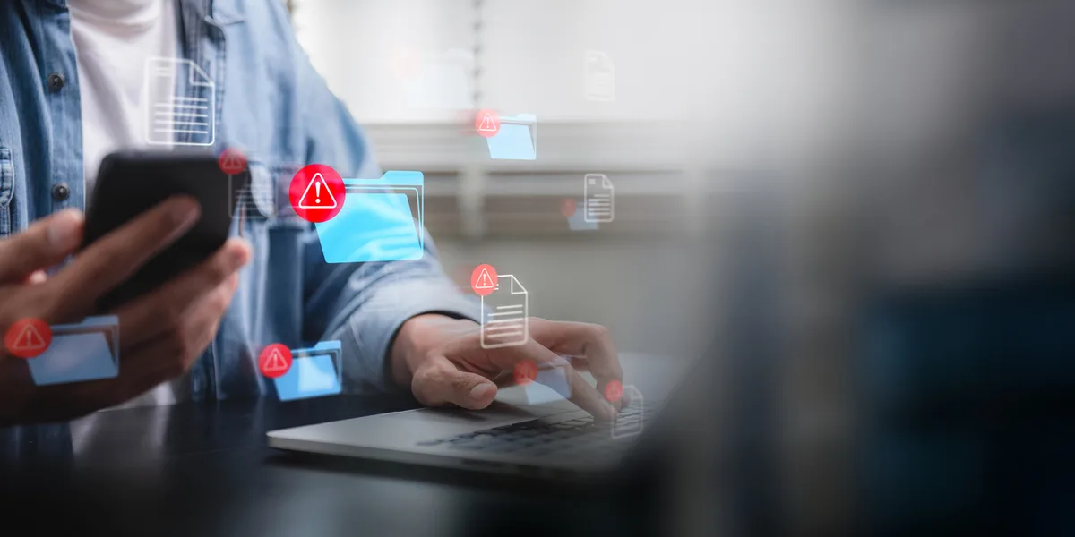 hacking and spam warning symbol on document file. Person using a smartphone and laptop with multiple cybersecurity alerts on a digital interface, highlighting potential data threats.