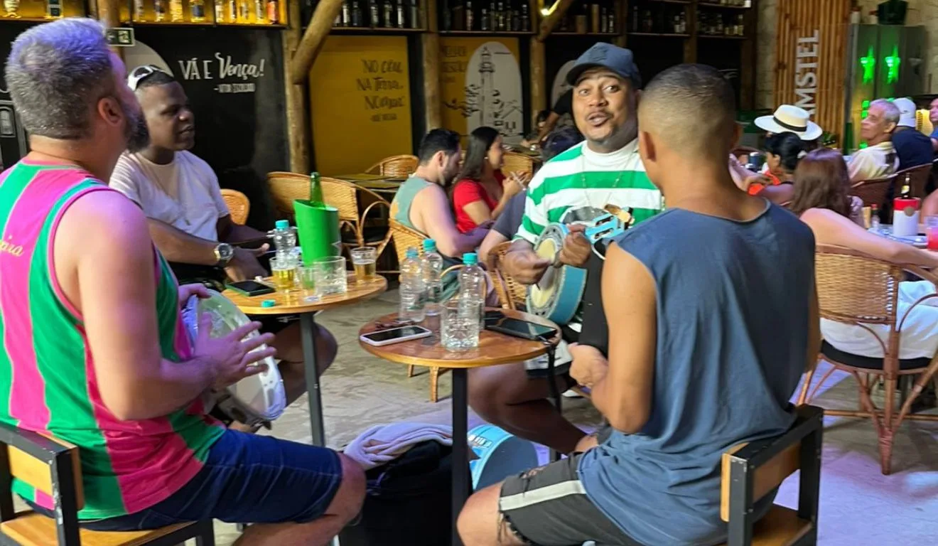 Três homens com instrumentos de pagode sentados ao redor de uma mesa