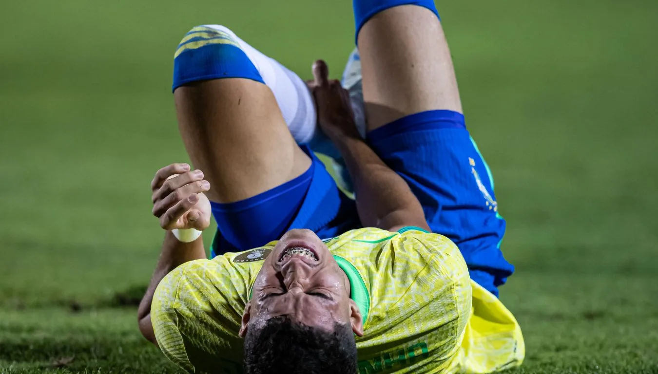 Jogador da seleção brasileira está caído no gramado, com a barrigada pra cima e os joelhos dobrados