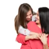 Waist up studio portrait of cute and playful schoolgirl embracing her mother. Happy family laughing background isolated over white.