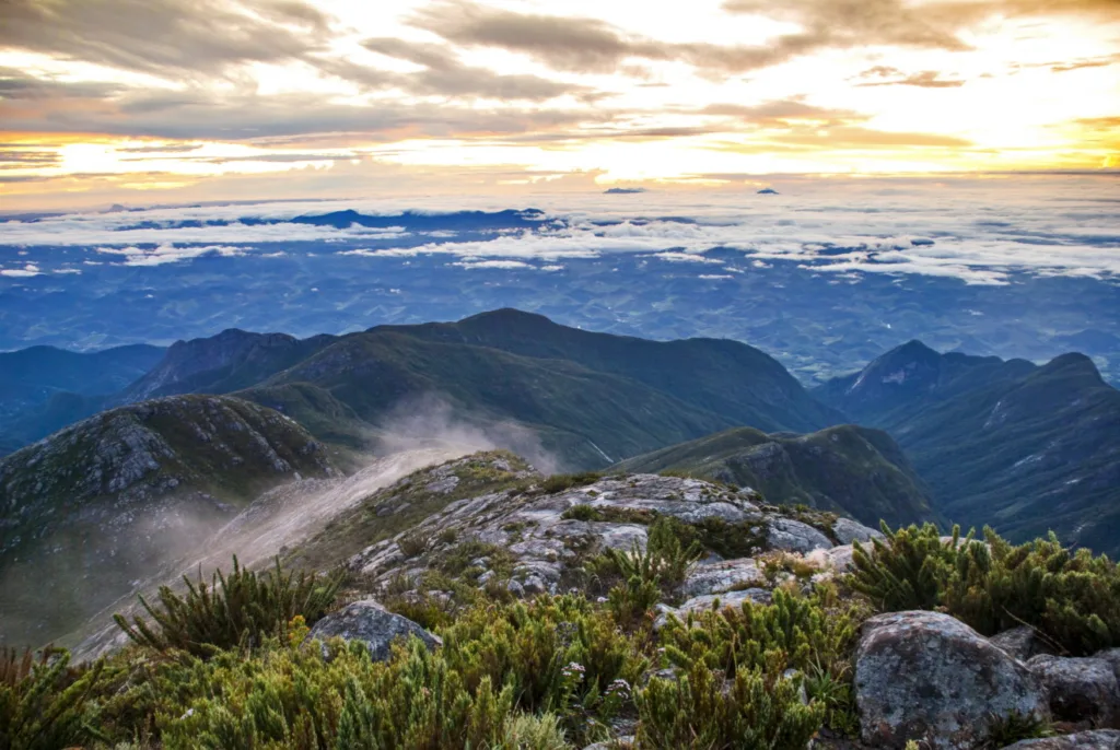 Vista panorâmica do horizonte a partir do Pico da Bandeira, com montanhas e nuvens compondo a paisagem