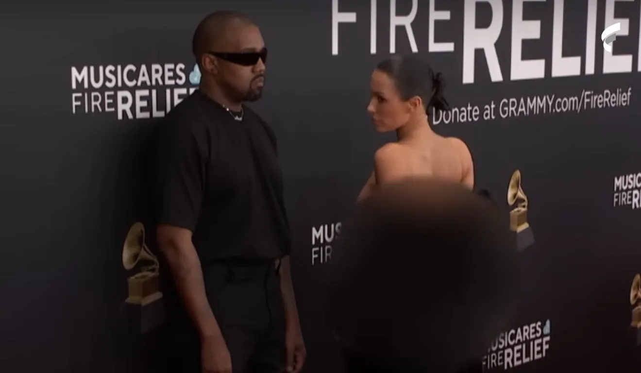 Kanye West e Bianca no tapete vermelho do Grammy 2025. Ele veste blusa e calça pretas e óculos escuros. Ela, revela um vestido transparente por baixo de um casaco de pele preto