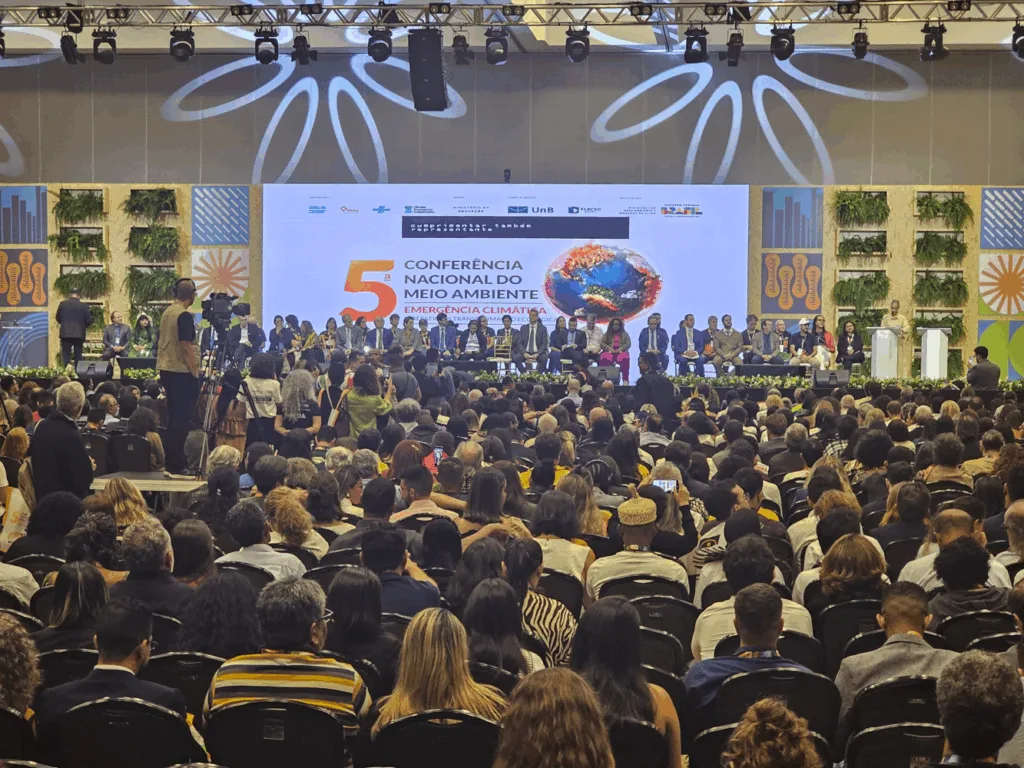 Delegações estaduais reunidas na plenária principal da conferência, com cartazes e faixas destacando causas locais