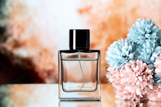 Imagem mostra perfume, com flores ao seu lado.