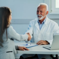 Happy mature doctor and his female patient shaking hands after medical appointment at clinic.