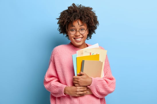 Imagem mostra aluna com vários livros e caderno no braço, representando estudos para Enem.