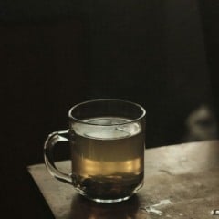 Mesa de madeira com xícara tranparente de chá de camomila.