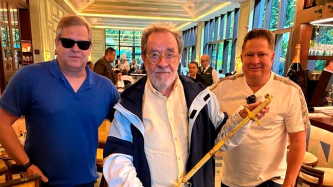 O escritor Fernando Morais, ao centro, segura espada doada pelos irmãos Gilberto e Edas Lopes. Crédito: Divilgação